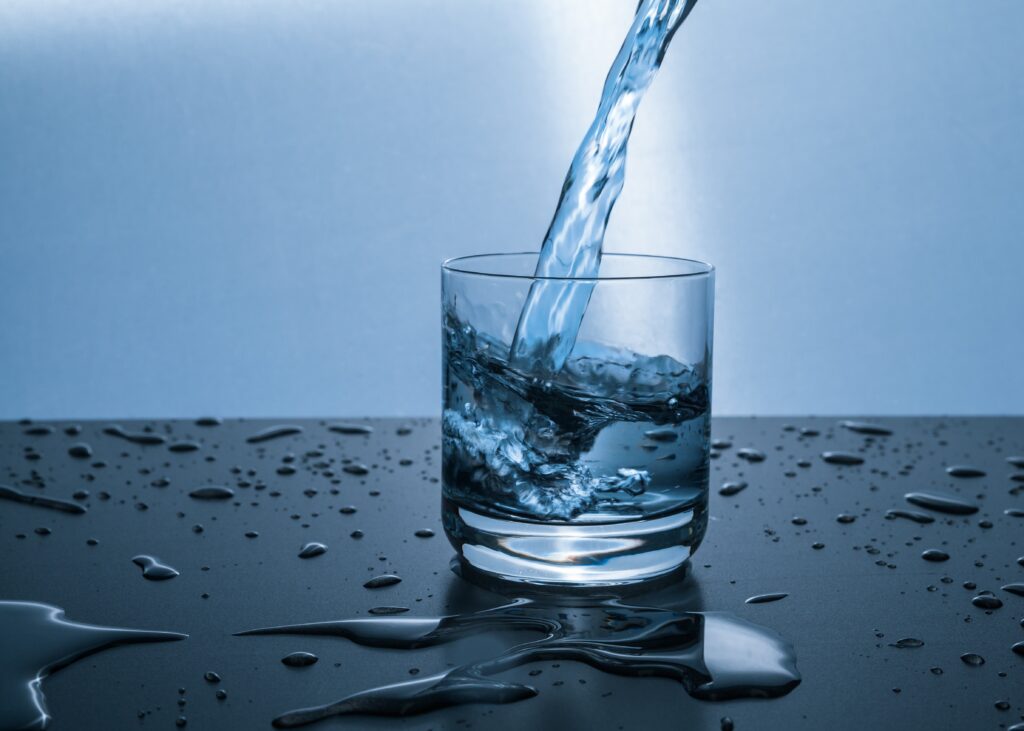 Water pouring into a glass on a table. Blue background.